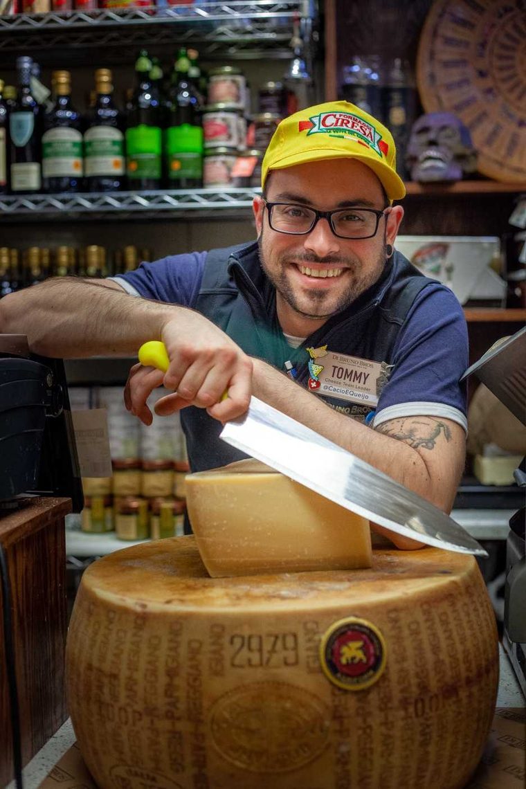 Tommy in a yellow cap cracking a wheel of Parmigiano Reggiano with a cheese knife
